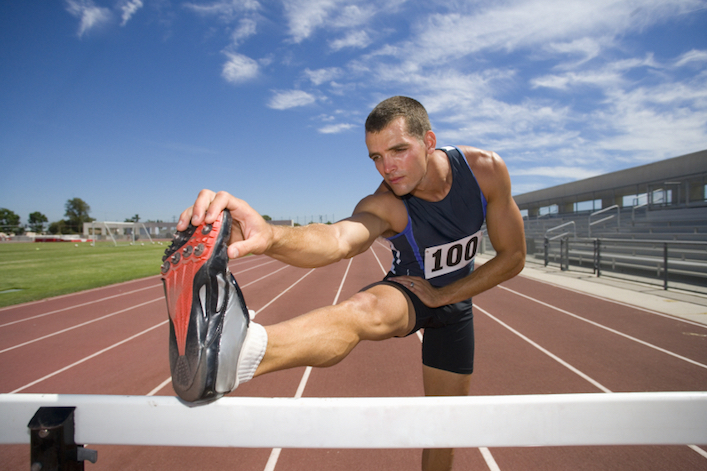 Male athlete stretching hamstrings, foot on hurdle, low angle view